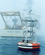Open ocean buoy used in the DART tsunami warning system with the research vessel Ronald H. Brown in the background in a mist-covered sea.